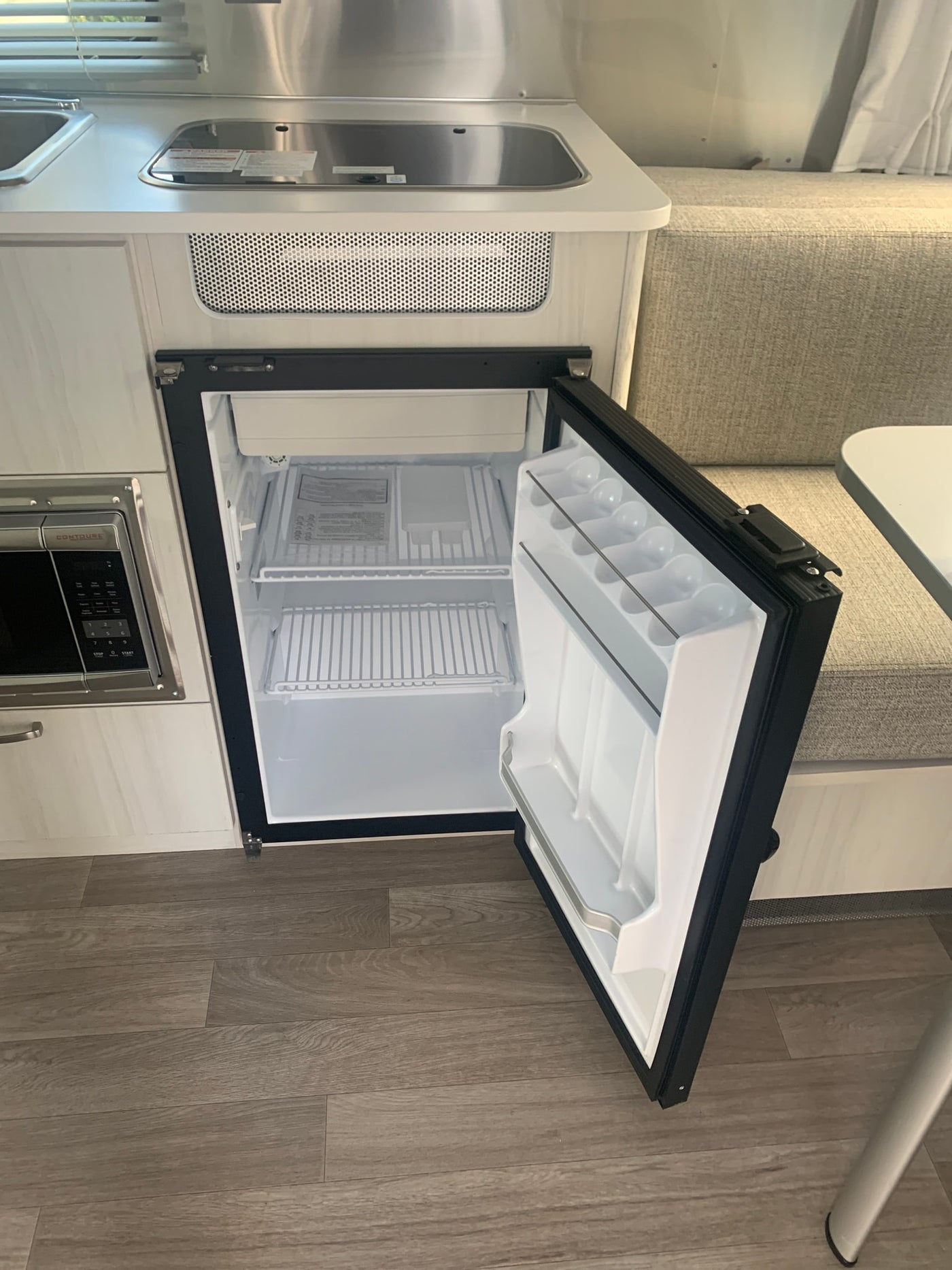 Explore your rv rental: a clean, open mini-fridge and microwave in a compact RV kitchen with a sink and dinette. — photo 11