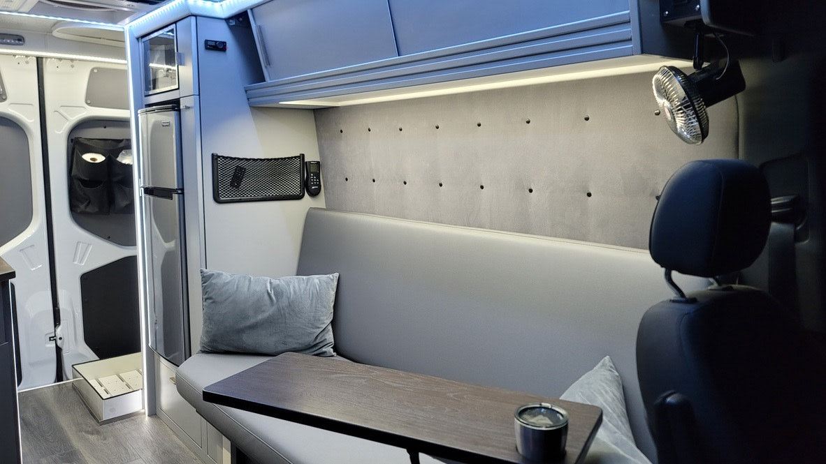 RV rental: Bright, organized camper interior. Features compact kitchen with fridge, comfy seating with table, fan & storage.