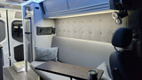 RV rental: Bright, organized camper interior. Features compact kitchen with fridge, comfy seating with table, fan & storage.