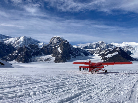 Stunning glacier landing by a red ski plane amidst towering snow mountains. An epic adventure, complementing your RV rental exploration.