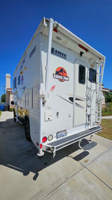 This unique white Lance truck camper, customized with a Jurassic Park logo, is parked on a driveway, ideal for RV rental adventures.