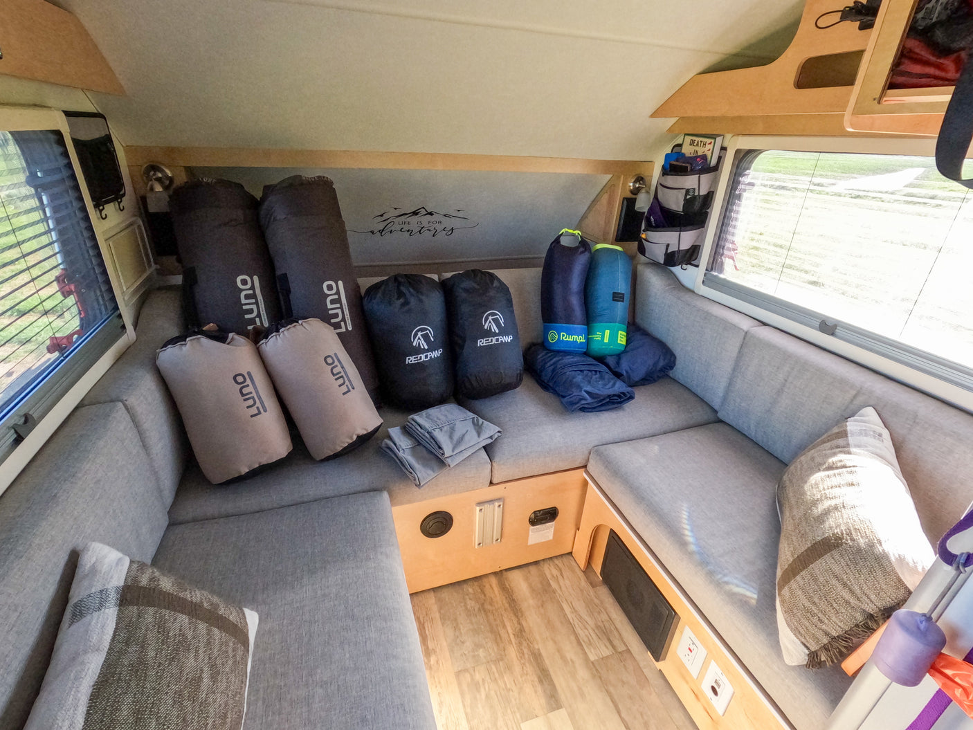 RV rental: Camper interior with grey upholstered seating, bundled Luno mattresses, Redcamp sleeping bags, & Rumpl blankets.