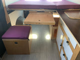 This RV rental's clever interior features a raised bed, pull-out table, cushioned storage, and compact kitchen counter.