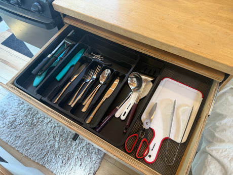 Open drawer in an RV rental kitchen showing organized cutlery, kitchen shears, and a small cutting board.