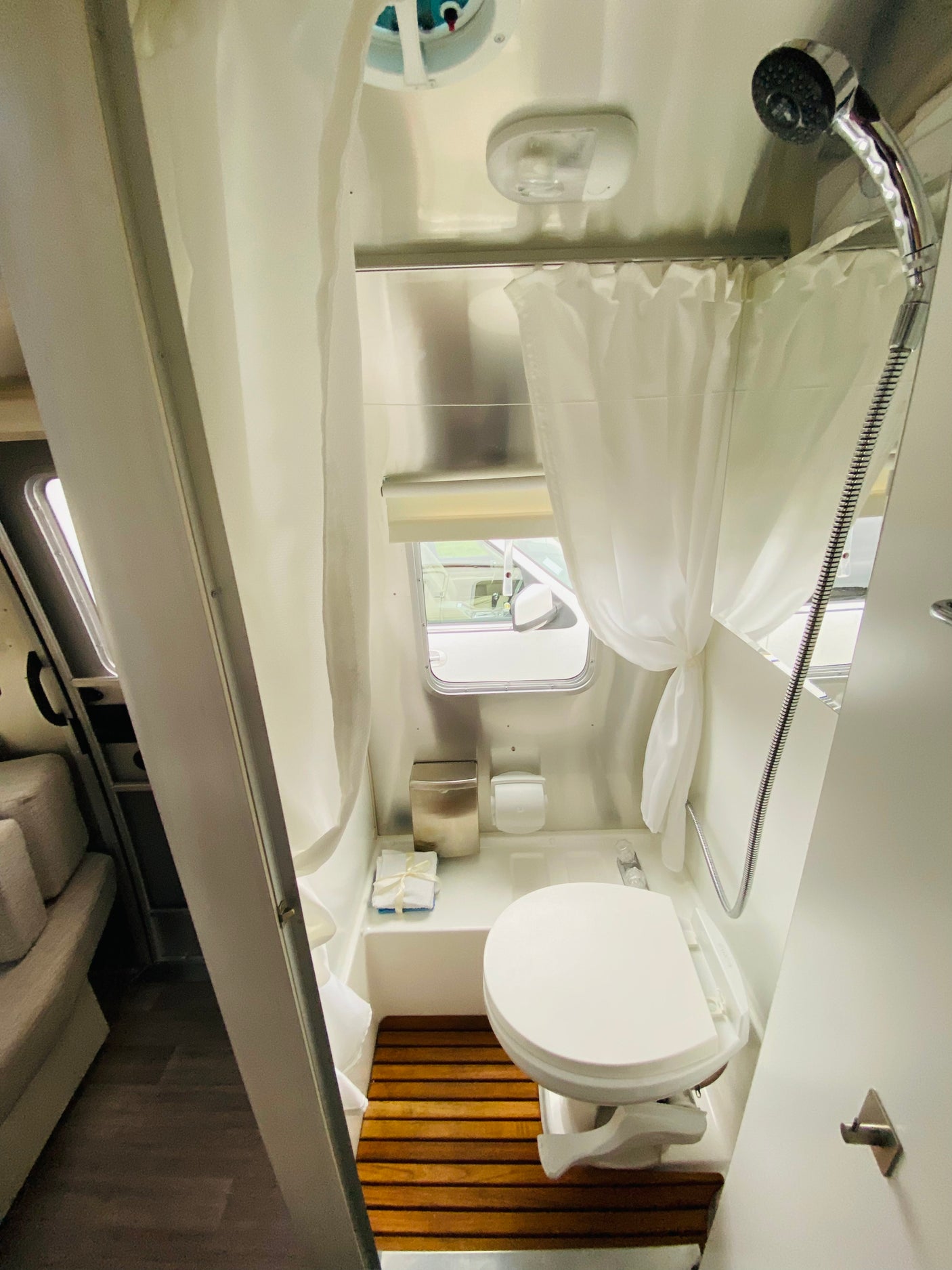Clean, compact RV rental bathroom showing a toilet, shower, wooden mat, and small window, ideal for comfortable travels.