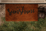 Inviting 'HEY SUNSHINE' doormat and sandals at the entrance of your cozy RV rental, surrounded by concrete and grass.