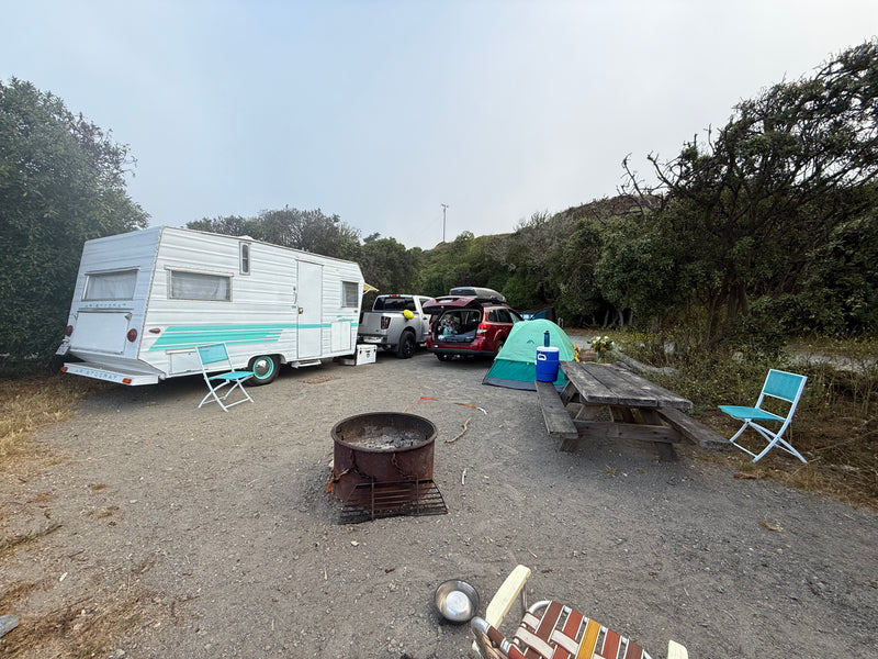 Enjoy an RV rental experience! A vintage trailer, tent, & vehicles parked at a rustic campsite with a fire pit. — photo 14
