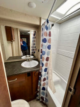 A compact and clean RV rental bathroom with a sink, large mirror, and shower/tub combo with a polka-dot curtain.
