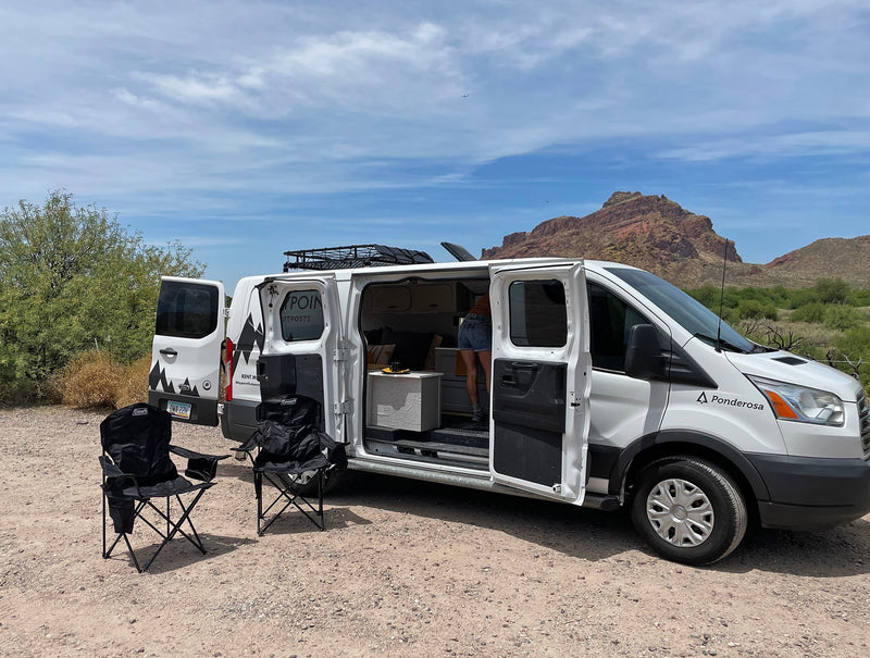 An RV rental camper van with open doors and outdoor chairs in a desert mountain setting, ready for adventure. — photo 7