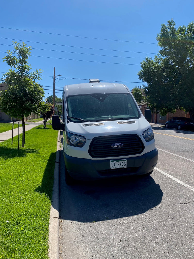  parked on a sunny day with green grass and trees.|Scenic RV rental: White camper van with doors open showing cozy interior & black dog. A tan dog stands outside in the grass.|Front view of a white Ford Transit camper van — photo 3