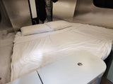Cozy RV rental bed with white sheets & pillows. Compact interior featuring a table & wall storage.