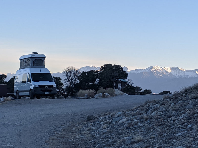 A white RV rental camper van is parked on a dirt road, offering stunning views of snow-capped mountains. — photo 1