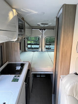 RV rental interior: compact kitchen with refrigerator, versatile bed/seating area, and rear windows.