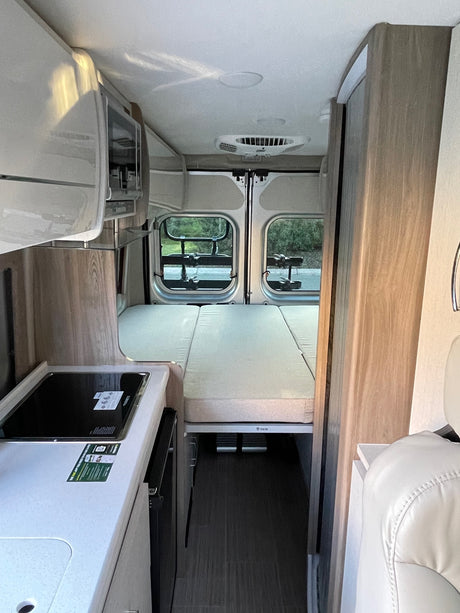 RV rental interior: compact kitchen with refrigerator, versatile bed/seating area, and rear windows.