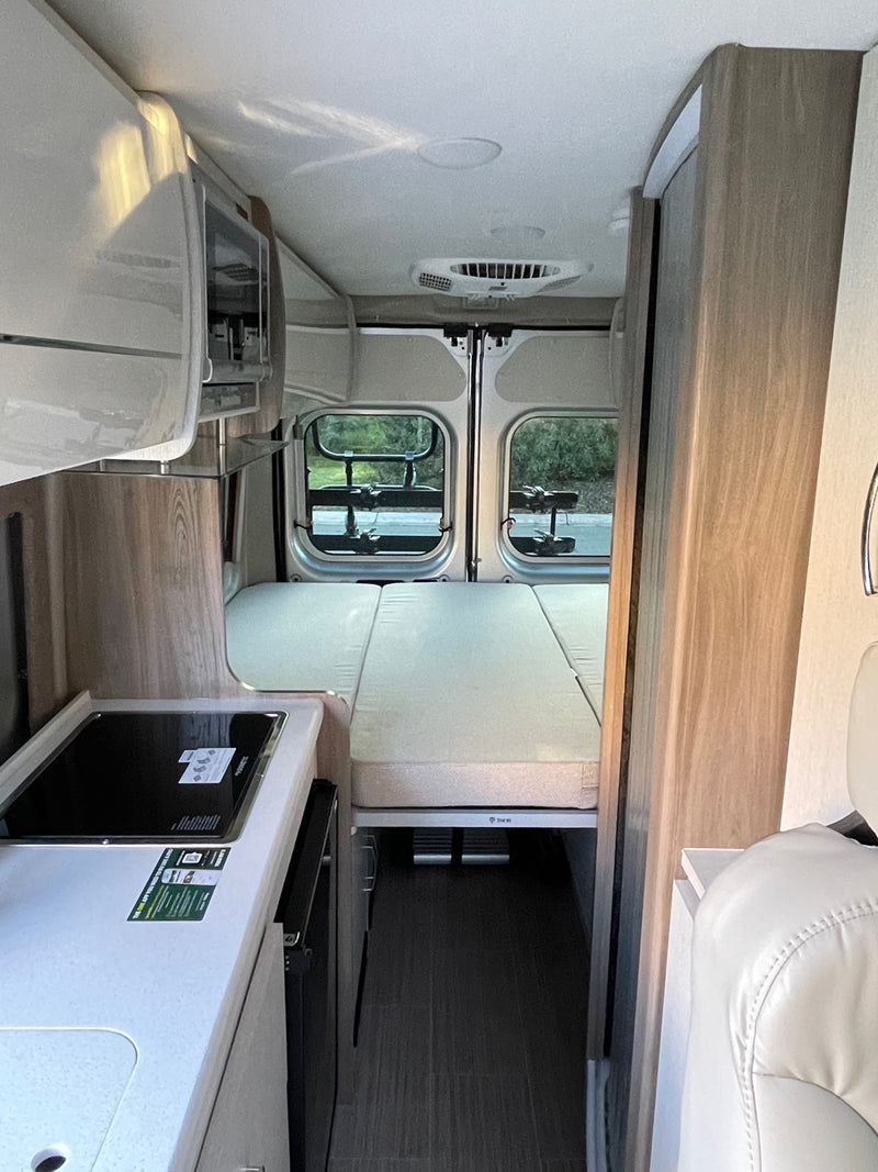 RV rental interior: compact kitchen with refrigerator, versatile bed/seating area, and rear windows. — photo 11