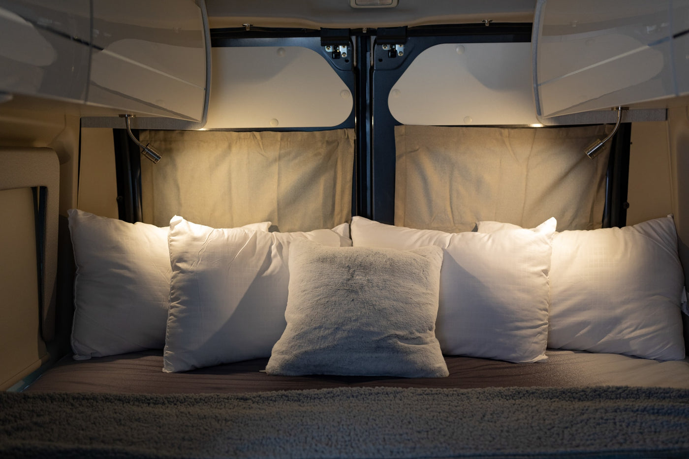  parked outdoors with a bike rack and pop-top.|Plush pillows and reading lights create a cozy RV rental bedroom. Overhead cabinets complete this comfortable — photo 16