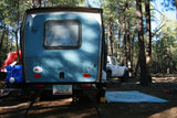 Blue RV rental trailer, tent, and pickup truck nestled in a sunny pine forest campsite. Enjoy outdoor adventures!