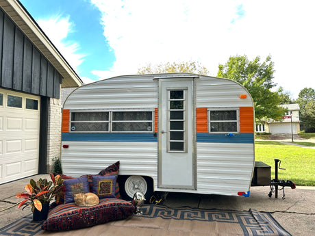 Retro RV rental parked, with a ginger cat sleeping on a patterned cushion and a potted plant.