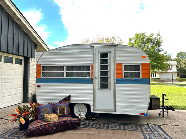 Retro RV rental parked, with a ginger cat sleeping on a patterned cushion and a potted plant.
