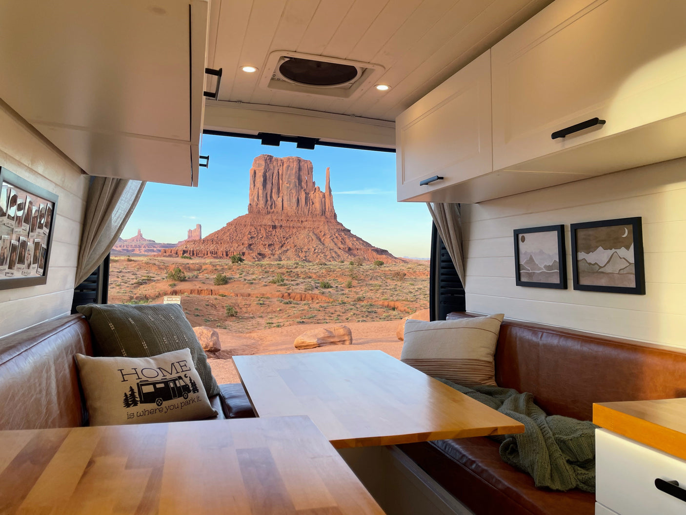 Cozy RV rental interior with brown leather seating, wooden tables, and a stunning open-door view of Monument Valley.