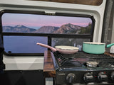 Crater Lake sunset from an rv rental window, featuring a Dometic stovetop with pink and teal cookware for a scenic meal.