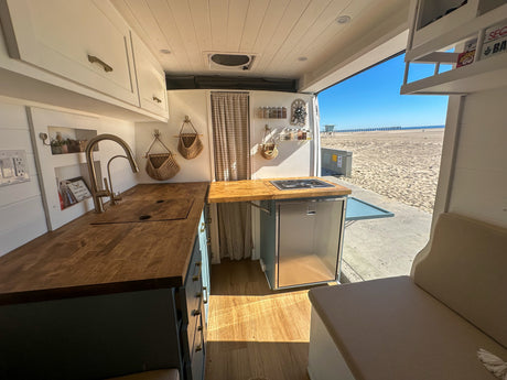 RV rental: Enjoy a bright camper van kitchen with wooden counters and fridge, open to a stunning beach and ocean view.