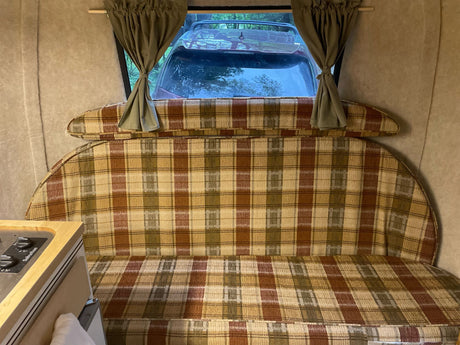 Inside a cozy RV rental: Plaid bench seating, window curtains, and a view of the outdoors. Great for camping adventures!