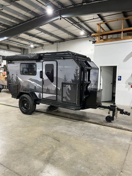 This rugged overland adventure trailer, perfect for RV rental, features a mountain graphic and robust off-road tires.
