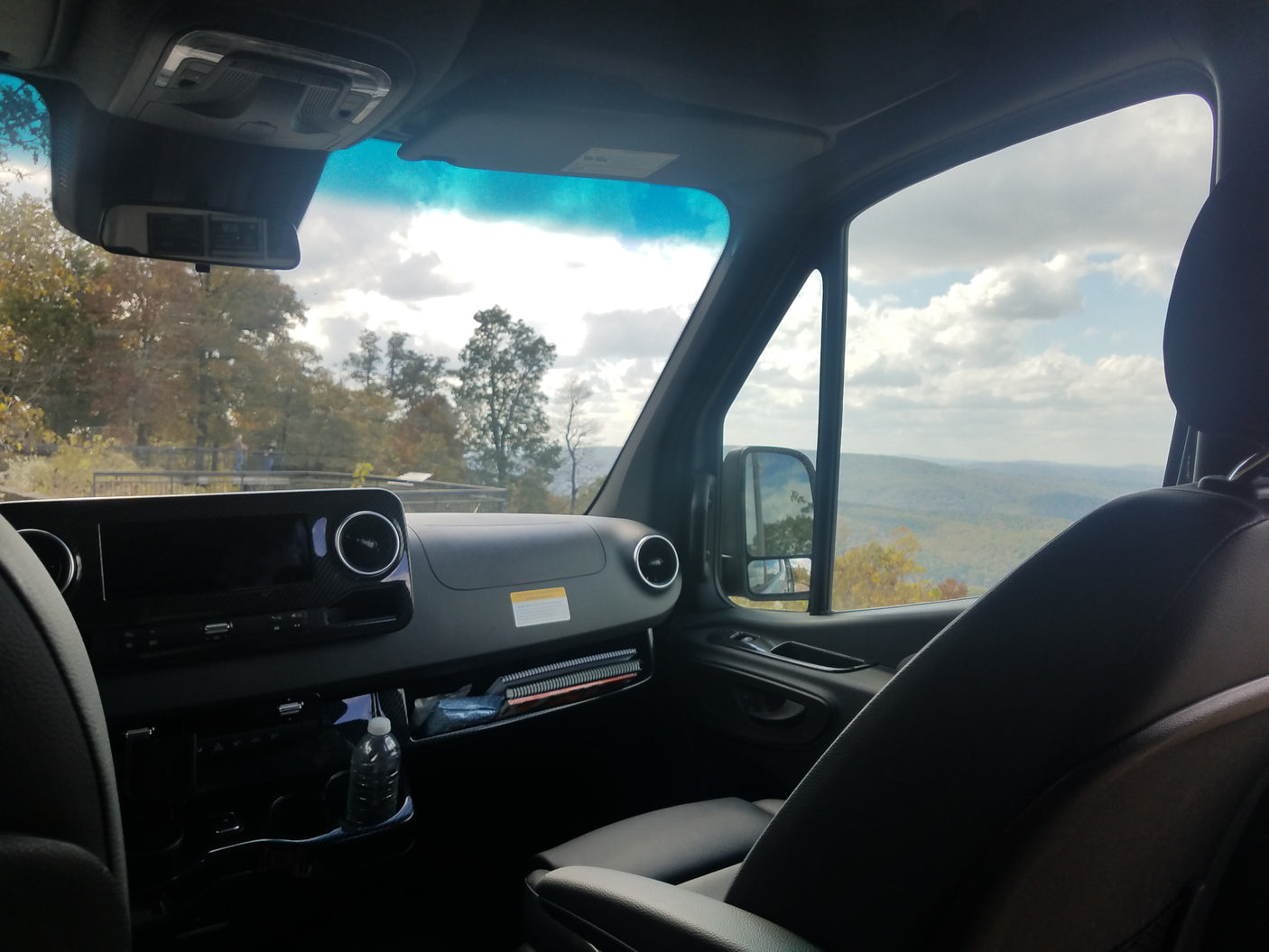 Inside an RV rental, a sleek dashboard and passenger seat offer a stunning view of mountainous landscapes and cloudy skies.