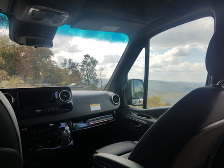 Inside an RV rental, a sleek dashboard and passenger seat offer a stunning view of mountainous landscapes and cloudy skies.