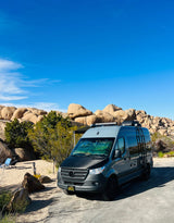 Gray Mercedes Sprinter **RV rental** parked in a sunny, rocky desert camp. Perfect for exploring national parks.