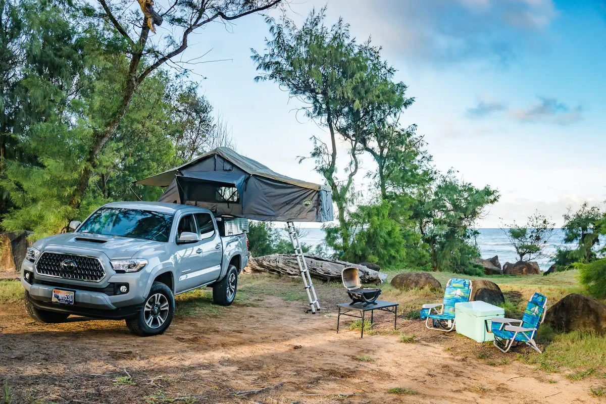  and grill set for evening camping.|Gray Toyota Tacoma pickup truck with a deployed roof-top tent — photo 2
