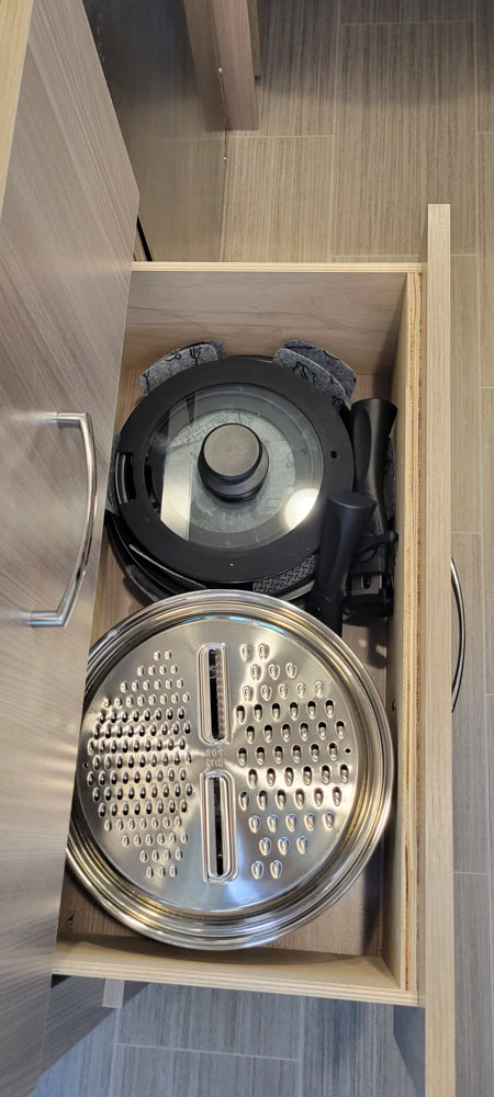RV rental compact kitchen storage: An open drawer showing stacked pots/pans with a glass lid and a large grater.