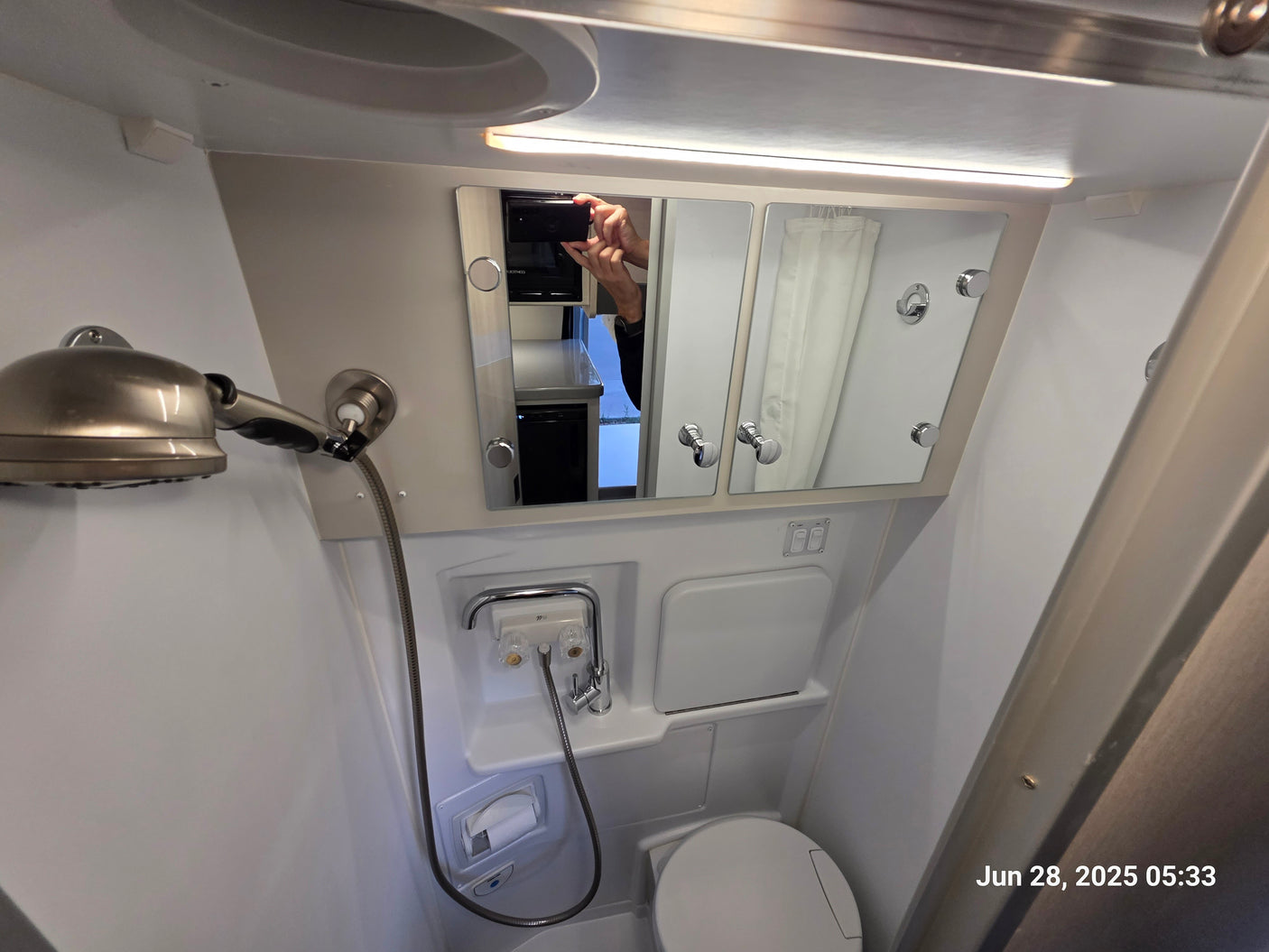 This image shows a compact RV rental wet bath, featuring a toilet, shower, sink, and a mirrored medicine cabinet.