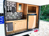 RV rental outdoor kitchen featuring a sink, stovetop, fridge, and mosaic backsplash. Ready for camping trips.