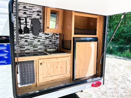 RV rental outdoor kitchen featuring a sink, stovetop, fridge, and mosaic backsplash. Ready for camping trips.