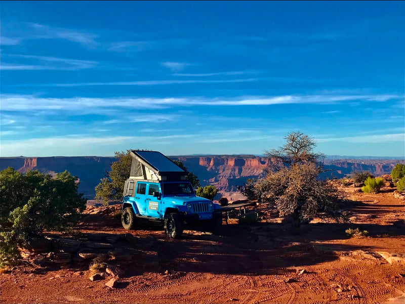 is parked with camping chairs before grand red cliffs.|Blue Jeep overlanding RV rental by a glowing canyon river — photo 9