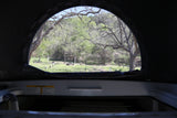 View from inside an RV rental: a peaceful campsite with lush trees and picnic tables.