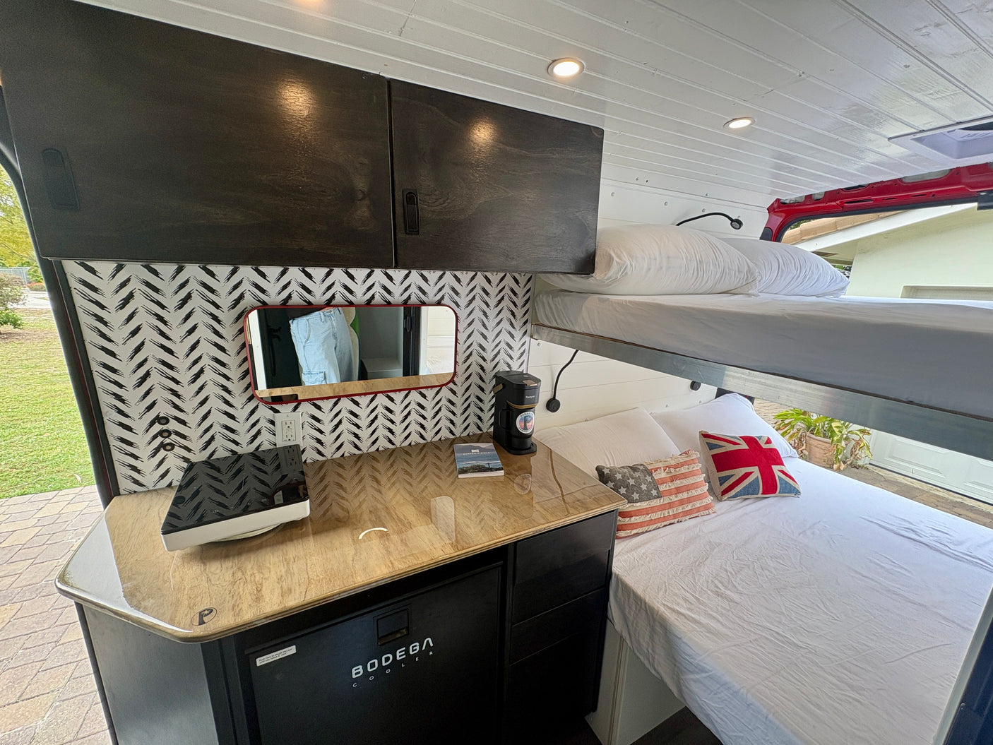 Compact rv rental interior featuring bunk beds, a modern kitchenette, and stylish overhead cabinets, perfect for van life.