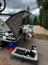 Camping with an RV rental: a compact teardrop trailer's outdoor kitchen and a resting dog. Scenic mountains beyond.