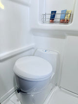 RV rental's clean white bathroom featuring a compact toilet, shower, and toiletries on a wall rack.