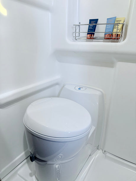 RV rental's clean white bathroom featuring a compact toilet, shower, and toiletries on a wall rack.