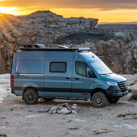An off-road Winnebago Revel 4x4 camper van, ideal for your next RV rental adventure, parked on a scenic cliff at sunset.