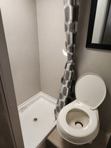 RV rental bathroom features a compact shower with geometric curtain and a white RV toilet with lid open.