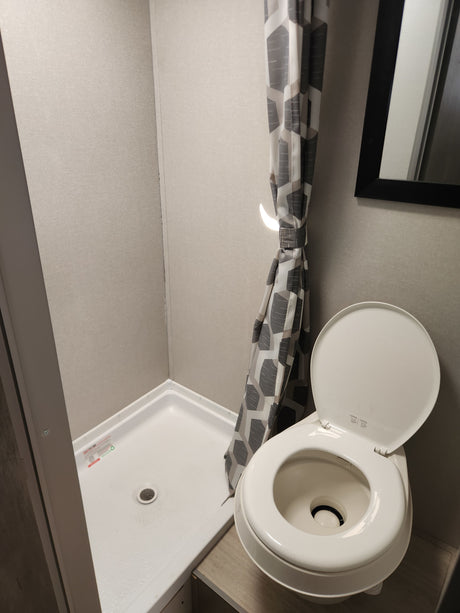 RV rental bathroom features a compact shower with geometric curtain and a white RV toilet with lid open.