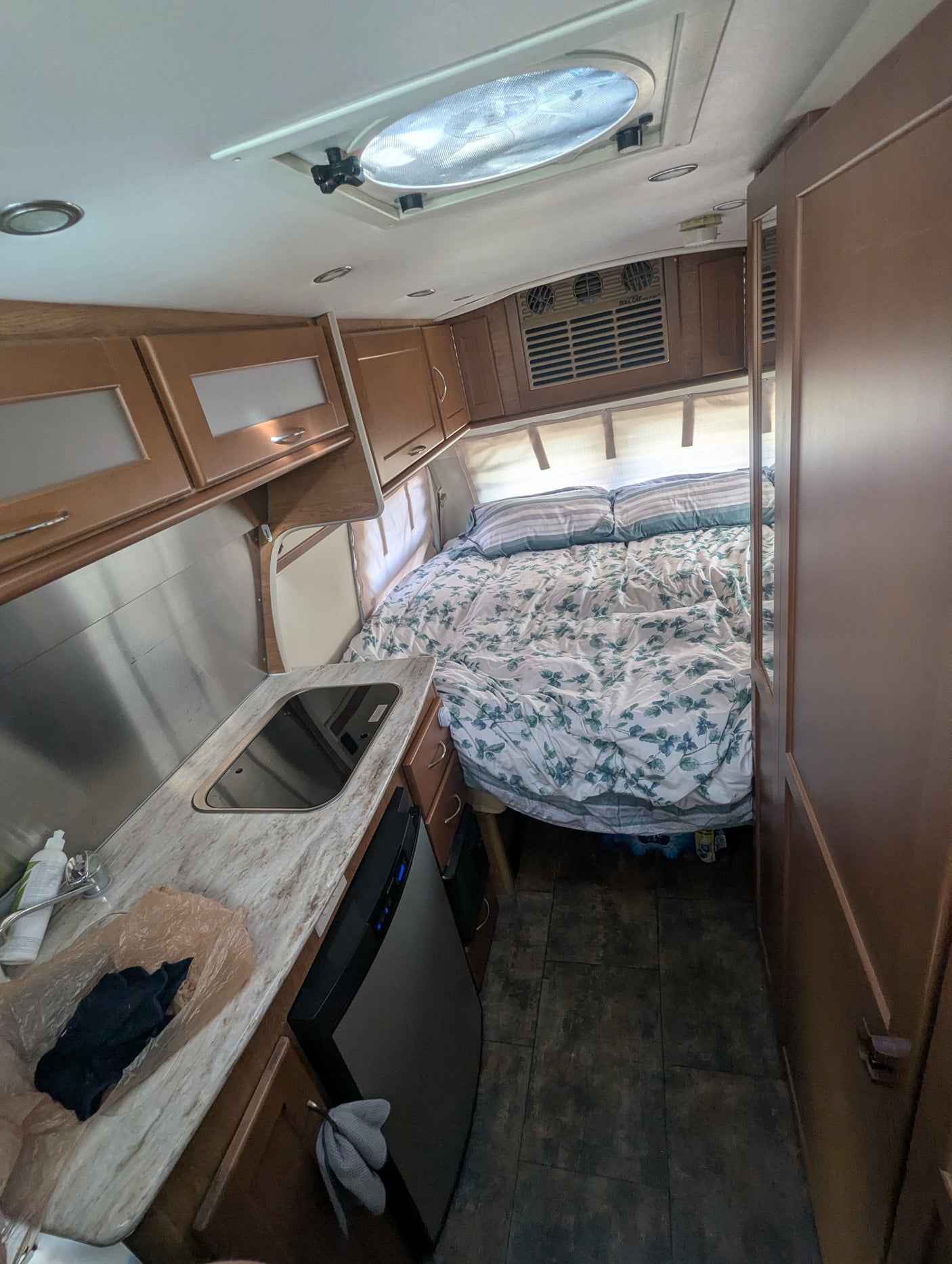 Inside an RV rental: full view of the bedroom area with a floral duvet, kitchenette with a sink, and mini-fridge.