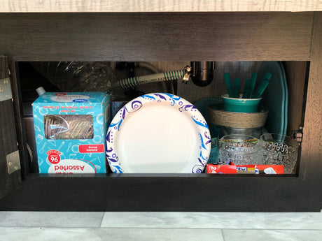 RV rental storage: under-sink cabinet with organized disposable plates, plastic cutlery, and other kitchen essentials.