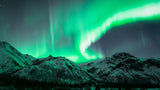 Aurora borealis brilliantly illuminates snow-capped mountains and starry skies, ideal for an RV rental journey.