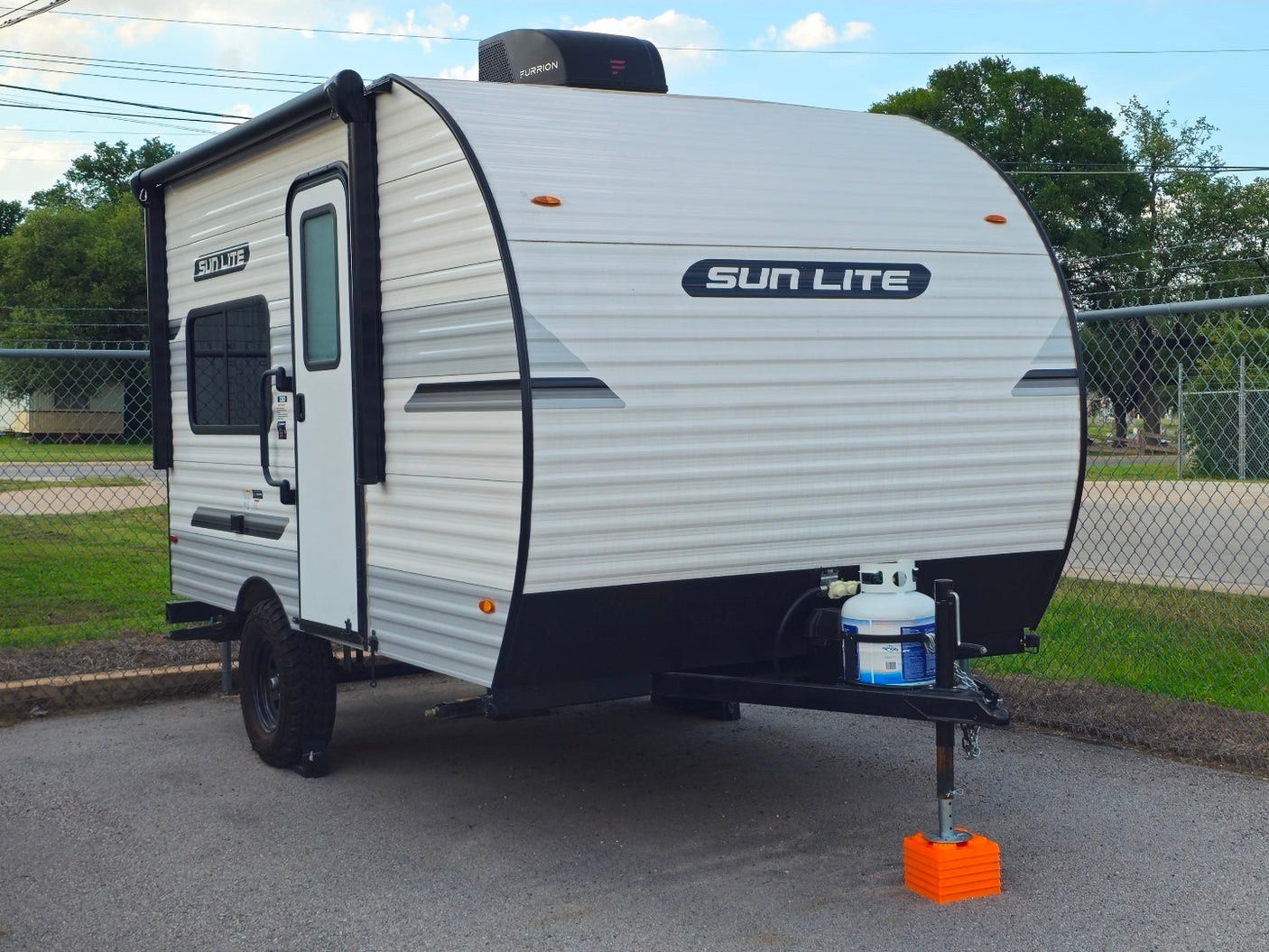 Compact white "SUN LITE" travel trailer rv rental with awning, propane tank, and rugged tires, parked on asphalt.