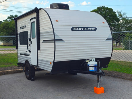 Compact white "SUN LITE" travel trailer rv rental with awning, propane tank, and rugged tires, parked on asphalt.